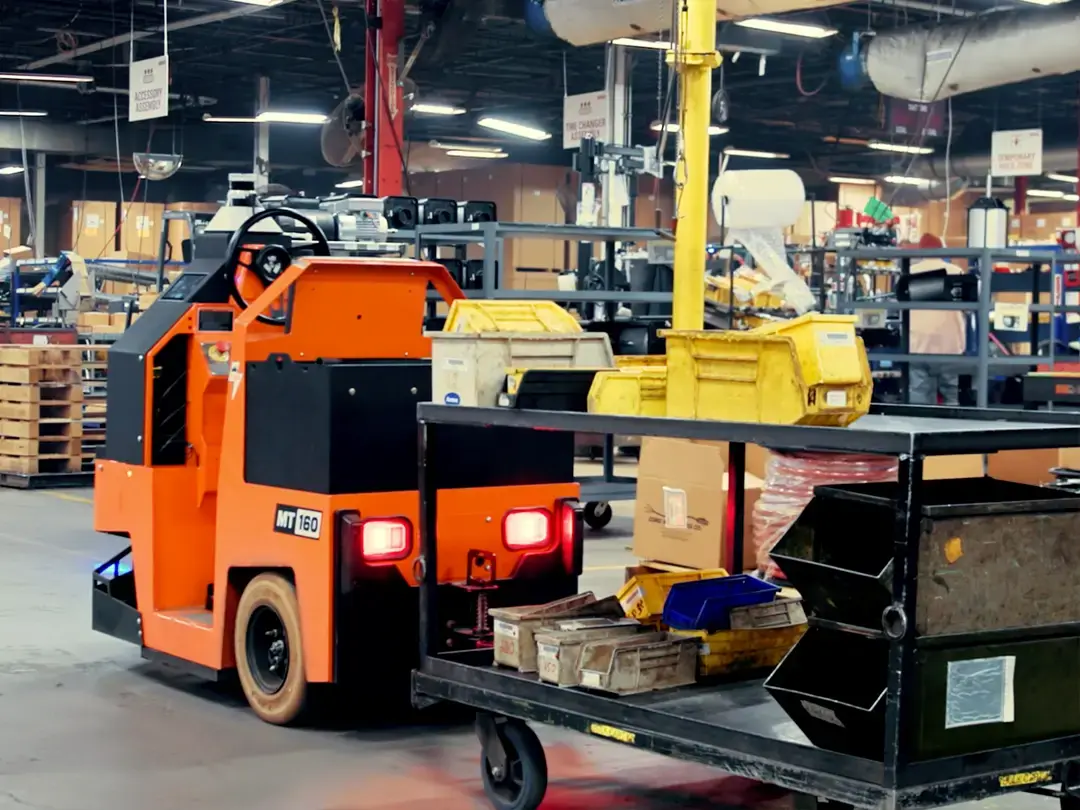 Autonomous tugger pulling a loaded cart past workstations